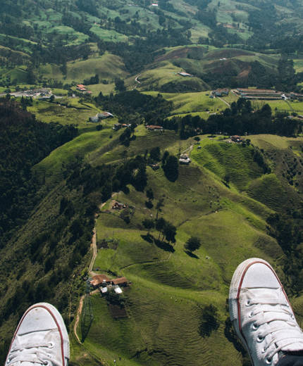 Aerial view from a skydiver's perspective as they fly over green hills below - KILROY