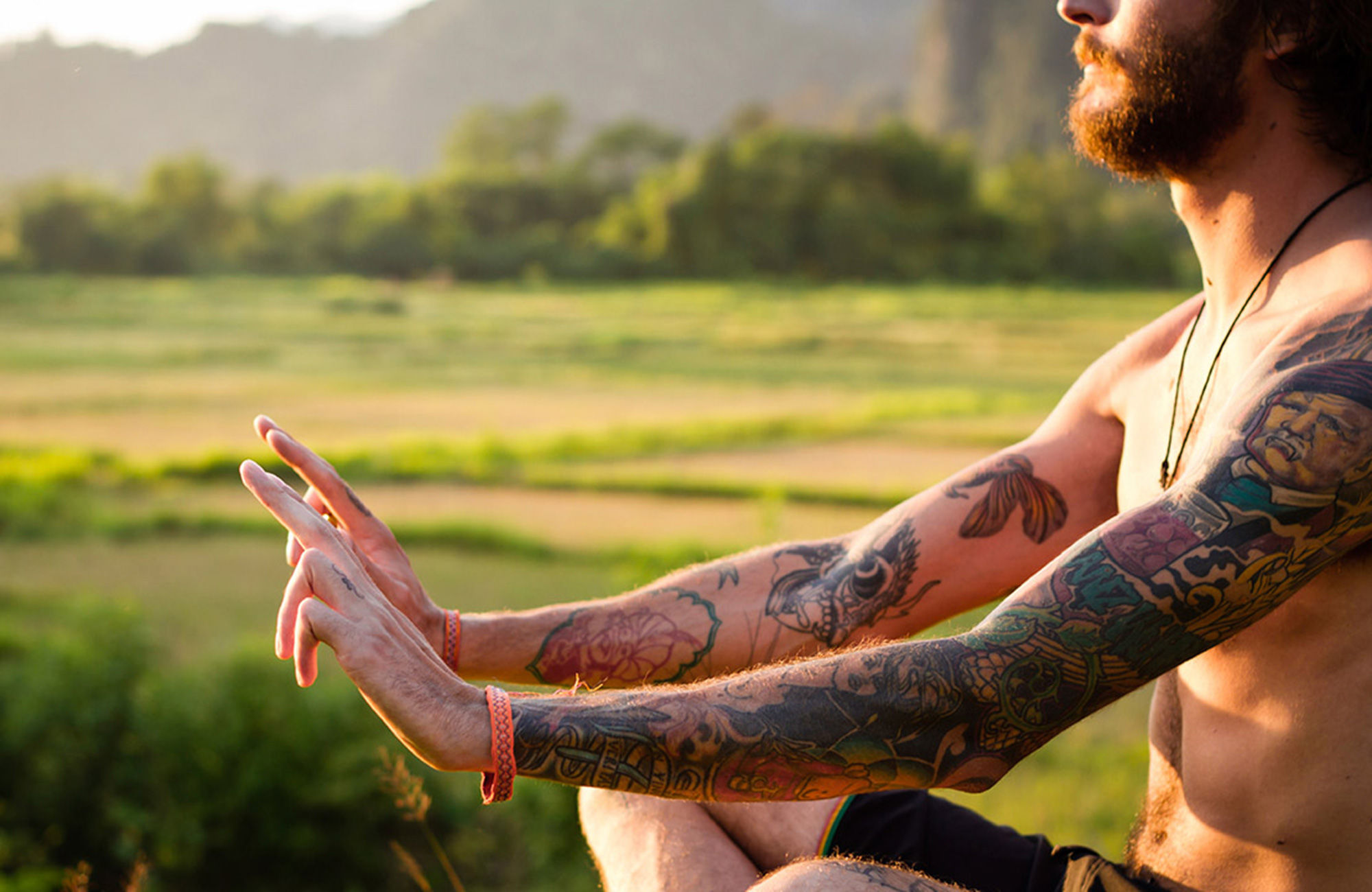 Image of a tattooed man practising yoga with rice paddies in the background - KILROY