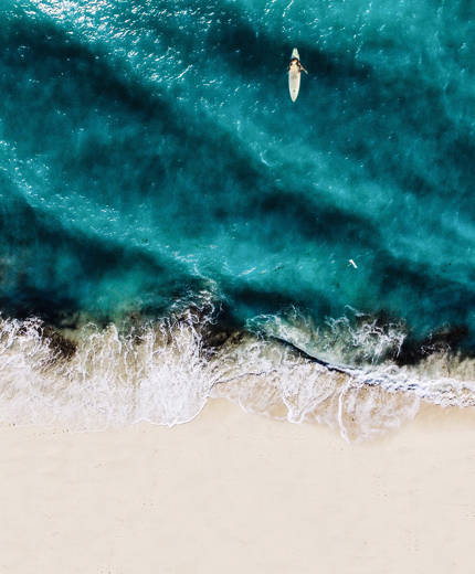 Aerial view of a surfer on the water as the waves break on a perfect sandy beach - KILROY