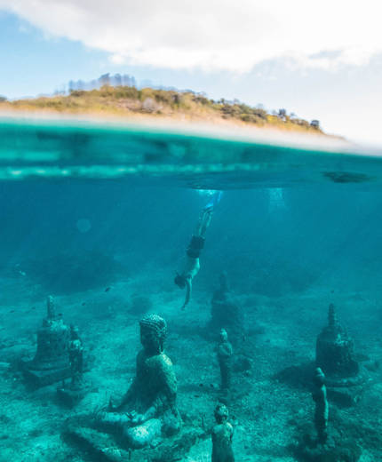 Image of a man diving under water with Buddhist temples littering the sea bed - KILROY