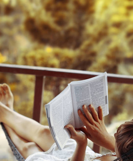 Image of a young woman reading a book while relaxing in a hammock - KILROY