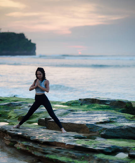 Image of a woman practising yoga on a rocky outcrop near the ocean - KILROY