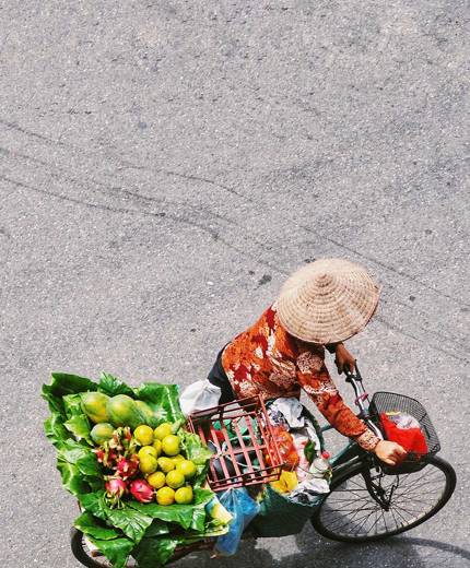 Image of a Vietnamese woman pushing a bike topped with baskets of fruit and vegetables - KILROY