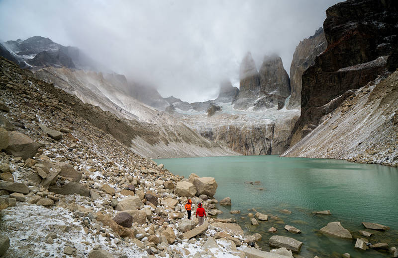Two hikers at a lake in Tierra del Fuego National Park, with the mountain tops covered by fog.
