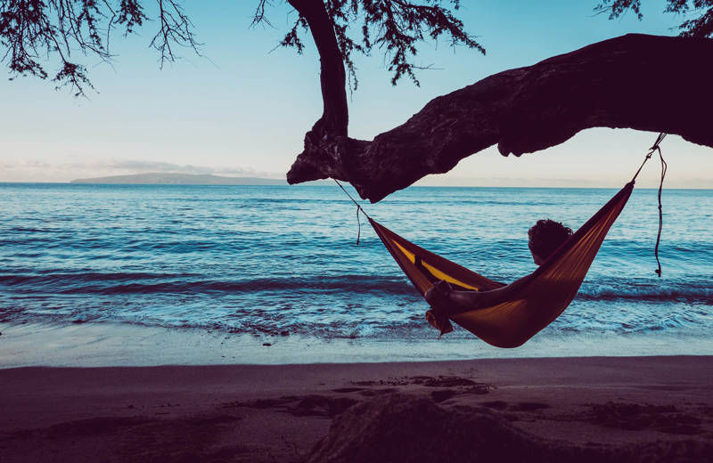 Image of a man relaxing in a hammock overlooking a beach - KILROY