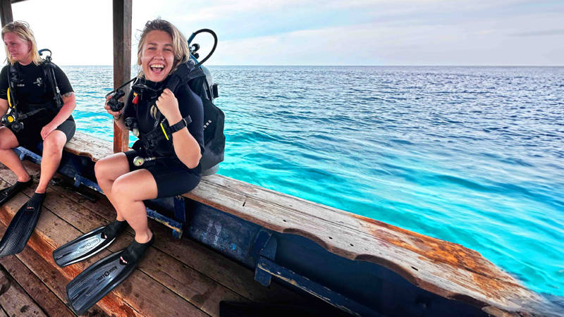 Image of a young female traveller in dive gear on a boat surrounded by blue sea - KILROY