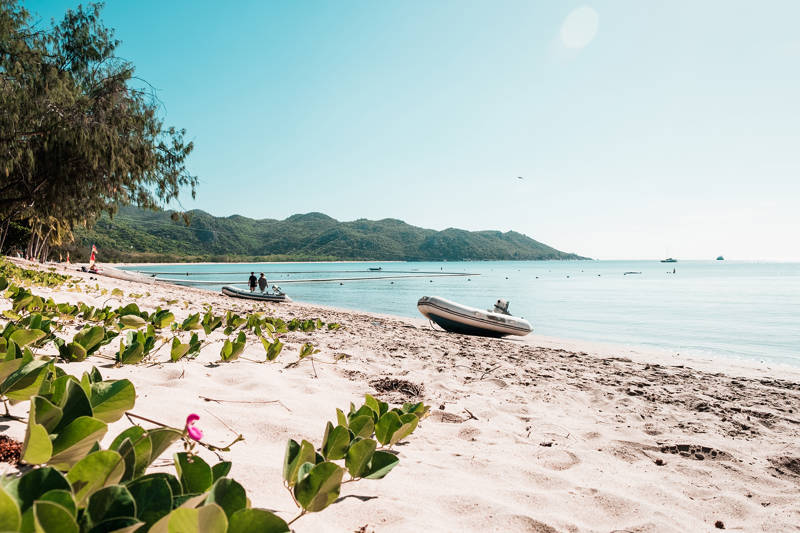 A sandy beach with two rubber boats, green hills and a very blue ocean, on Magnetic Island