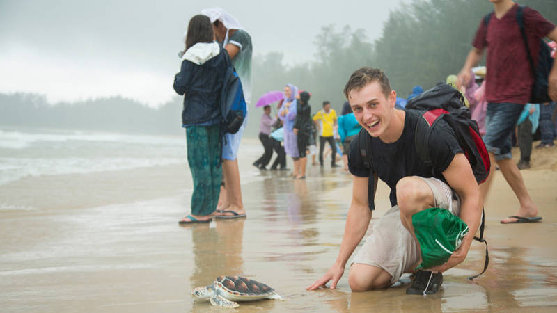 Image of a young man beside a turtle on a volunteer project in Thailand - KILROY