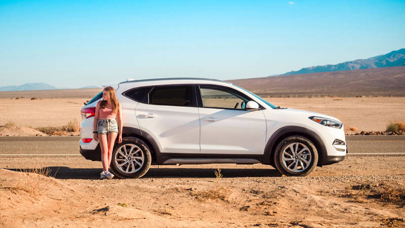 Image of a young female traveller standing by a car in Death Valley in California- KILROY